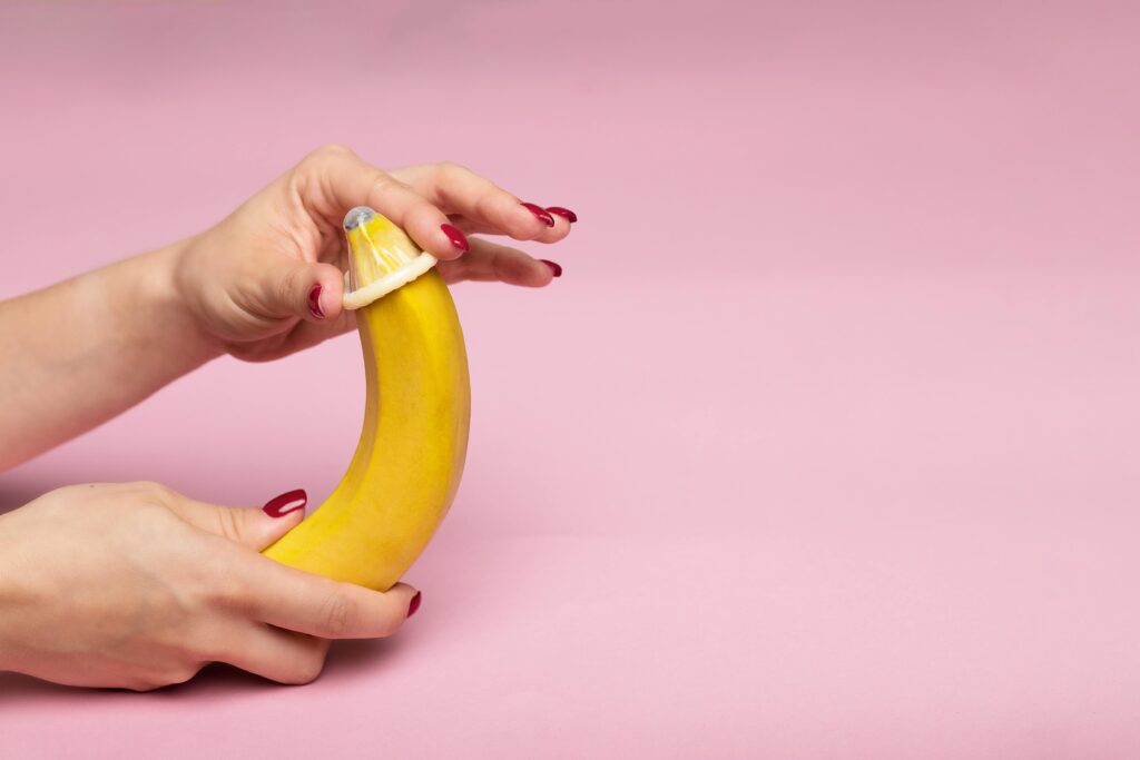 Close-up of hands demonstrating condom application on a banana, symbolizing safe sex education.